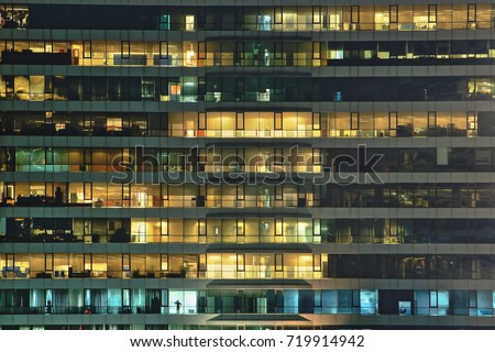 multi-storey office building at night with worker working overtime. late night at office. lighting and working people within. Late night overtime in a modern office building