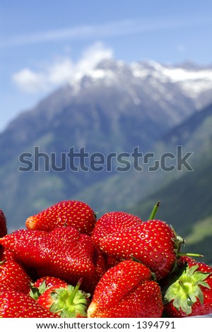 A pile of strawberries in front of an alpine backdrop; mountain out of DOF