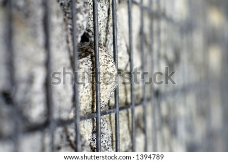 A single rock in a steelcage tries to break out; very shallow DOF with focus on tip of stone