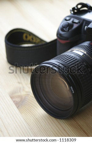 Debadged Digital SLR Camera. Shallow DOF, focus on the lens grip. Wood grain background.