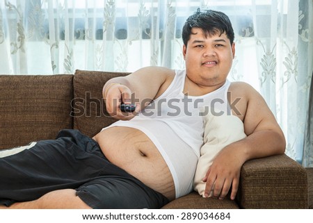 Overweight asian guy sitting on the couch with remote in hand trying to watch some TV
