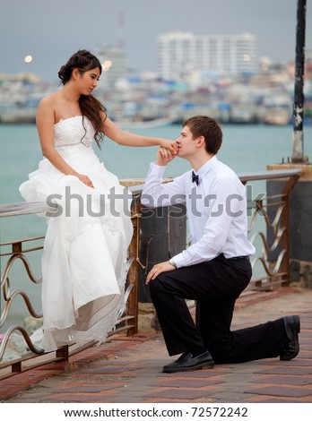 Newly married knee kisses a hand beside the sea