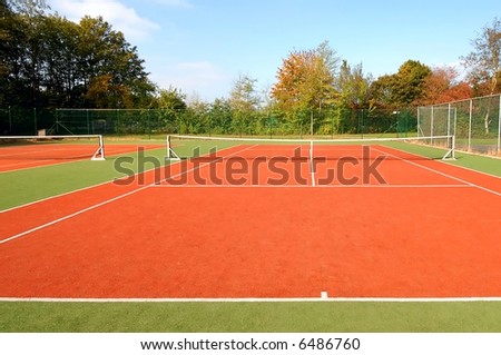 tennis court under blue sky, with autumn trees on the side.