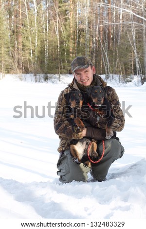 The man (Popov Dmitry) holds on hands of two hunting dogs Jagdterriers in the winter, looks in the camera