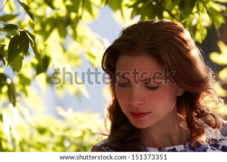 The beautiful girl in a foliage border thoughtfully looks down