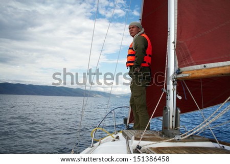 The man in a life jacket costs on a yacht nose, peering afar.