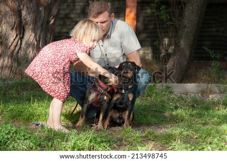 The fair-haired girl stretches something to two dogs terriers with hand bells under supervision of the father