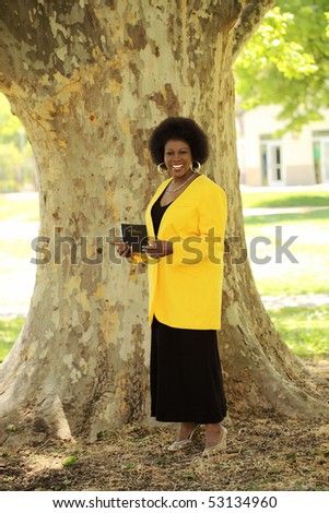 Older Black woman outdoors under tree holding Bible