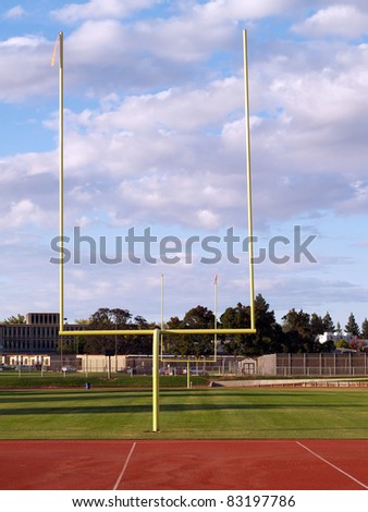 Yellow goal posts empty football field daytime white clouds