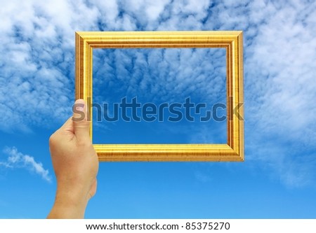a hand is holding a gold photo frame against the blue sky
