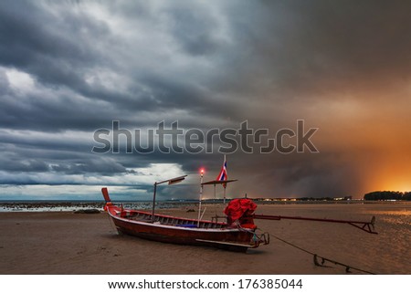 Sunset at tropical beach. Evening sea landscape with Thai traditional boat under dramatic stormy sky. Thailand