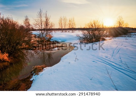 Winter sunset in winter field with small river