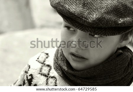 Boy in cap,  sweater and  scarf mistrustfully looks aside/I don\'t  trust