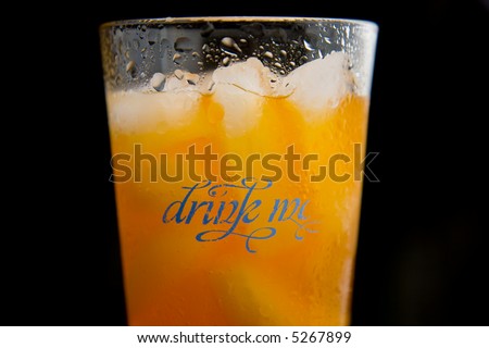 Drink of orange soda with some text on the glass that says drink me