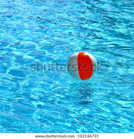 Beach ball floating in a pool with small waves reflecting in the summer sun