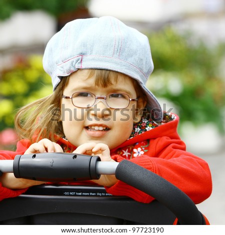 Beautiful little girl wearing glasses 3 years old in denim jeans cap and red jacket