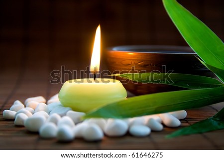 Composition with white zen stones, burning candle, bamboo leaves and clay bowl with tea symbolizing harmony, calmness and relaxation