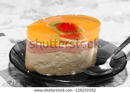Delicious jelly cake with kiwi and cherry resting on the plate with a spoon.