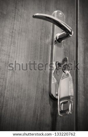 The key inside the keyhole of a gilded handle of hotel room. Black and white