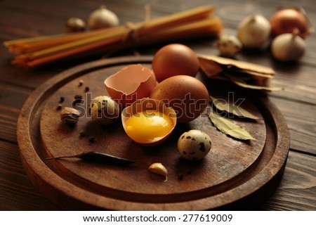 Various eggs and spices on a rustic aged wooden carving board at wooden tabletop