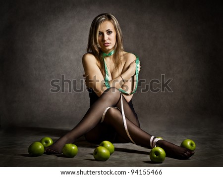 Diet Concept - a beautiful blondie topless wound herself with a centimeter measuring tape sitting at the floor in front of some green apples