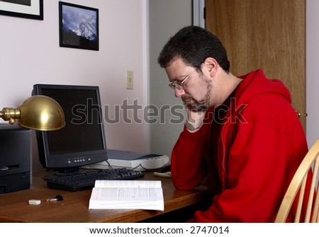 Middle-aged man reading a book in front of the computer.