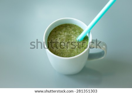 A cup of a green smoothie with a blue straw inside, healthy drink and food that fits for a diet