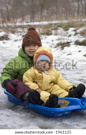 sister and brother tobogganing in a cold winter day