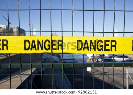 Yellow tape on a fence, with danger written on it.