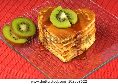 Heart-shaped pancakes with syrup and kiwi fruit on a transparent glass dish over a red background. A perfect breakfast for Valentine\'s Day