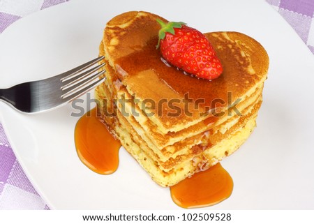 Heart-shaped pancakes with syrup and a strawberry on a white dish. A perfect breakfast for Valentine\'s Day