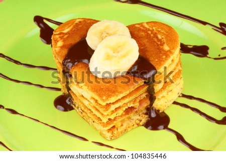 Heart shaped pancakes with chocolate sauce and banana slices on a green dish. A perfect breakfast for Valentine\'s Day.