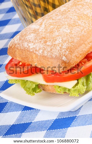 Close-up of an italian panino (sandwich) with freshly baked ciabatta bread, lettuce, cheese and tomato. In the background a glass of beer. Selective focus.