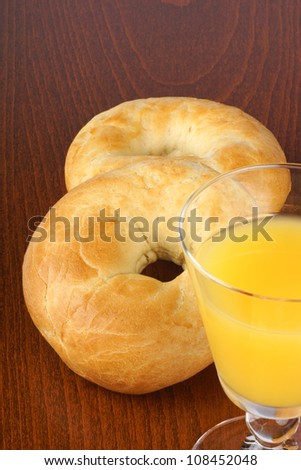 Two plain bagels and a glass of juice over a wooden background. Selective focus.