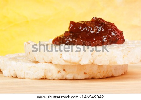 Closeup of two rice cakes with jam on a wooden cutting board over a yellow background