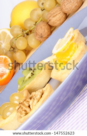 Assorted mini fruit tarts on a ceramic plate with fruit in the background. Selective focus.