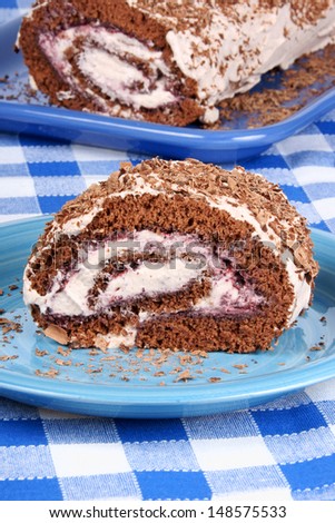 Chocolate swiss roll cake with berries jam and whipped cream over a chequered background.