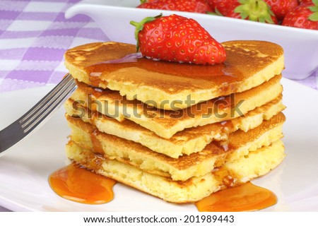Heart-shaped pancakes with syrup and a strawberry on a white dish. A perfect breakfast for Valentine\'s Day