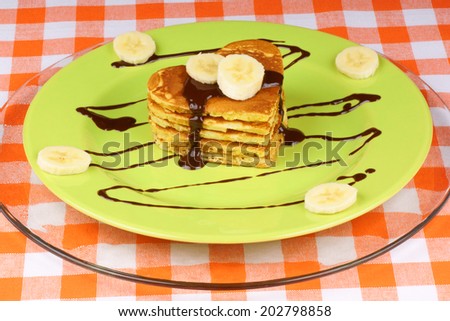 Heart shaped pancakes with chocolate sauce and banana slices on a green dish. A perfect breakfast for Valentine\'s Day.