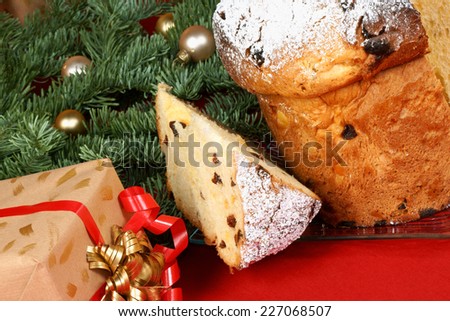 Panettone the italian Christmas fruit cake and a Christmas present under the Christmas tree, over a red background. Selective focus.