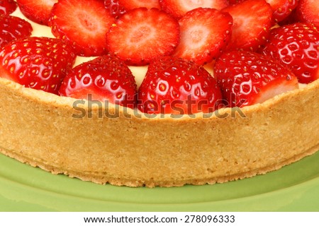 Closeup of a handmade strawberry and custard tart on a green dish.