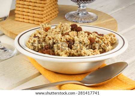 Healthy breakfast composed of a bowl of crunchy oat clusters with raisins, a glass of milk over a wooden background. Selective focus.