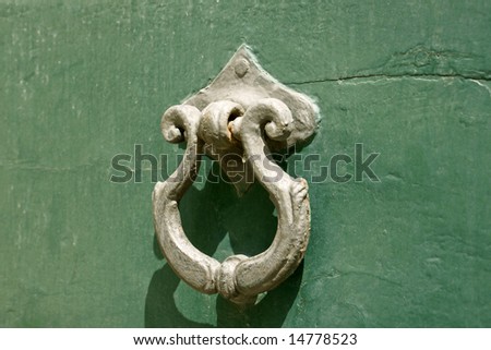 Ancient bronze door knocker over green painted wood