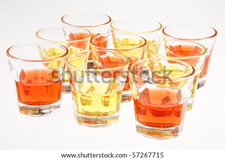 Closeup of some orange and yellow drinks served in mini glasses over a white background