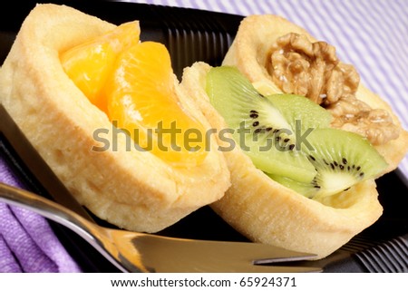 Closeup of some mini fruit tarts served on a black plate with dessert fork. Selective focus.