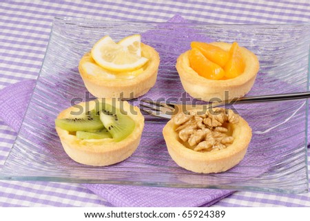 Closeup of some mini fruit tarts served on a glass plate with dessert fork. Selective focus.
