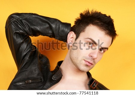 Serious young man with black leather jacket looking at camera over a yellow background.