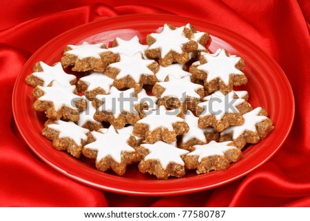 Closeup of some cinnamon star cookies (in german Zimtsterne), typical german and swiss Christmas cookies on a red plate over a red background.