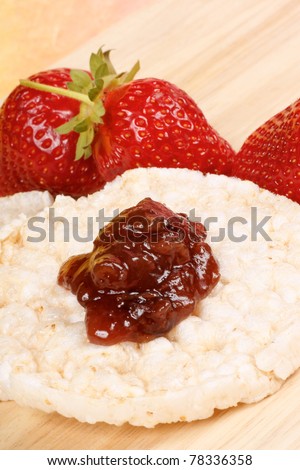 Closeup of two rice cakes with jam and some fresh strawberries on a wooden background for an healthy breakfast