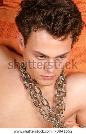 Portrait of a young man with blue eyes and brown hair with a chain around his neck among orange pillows